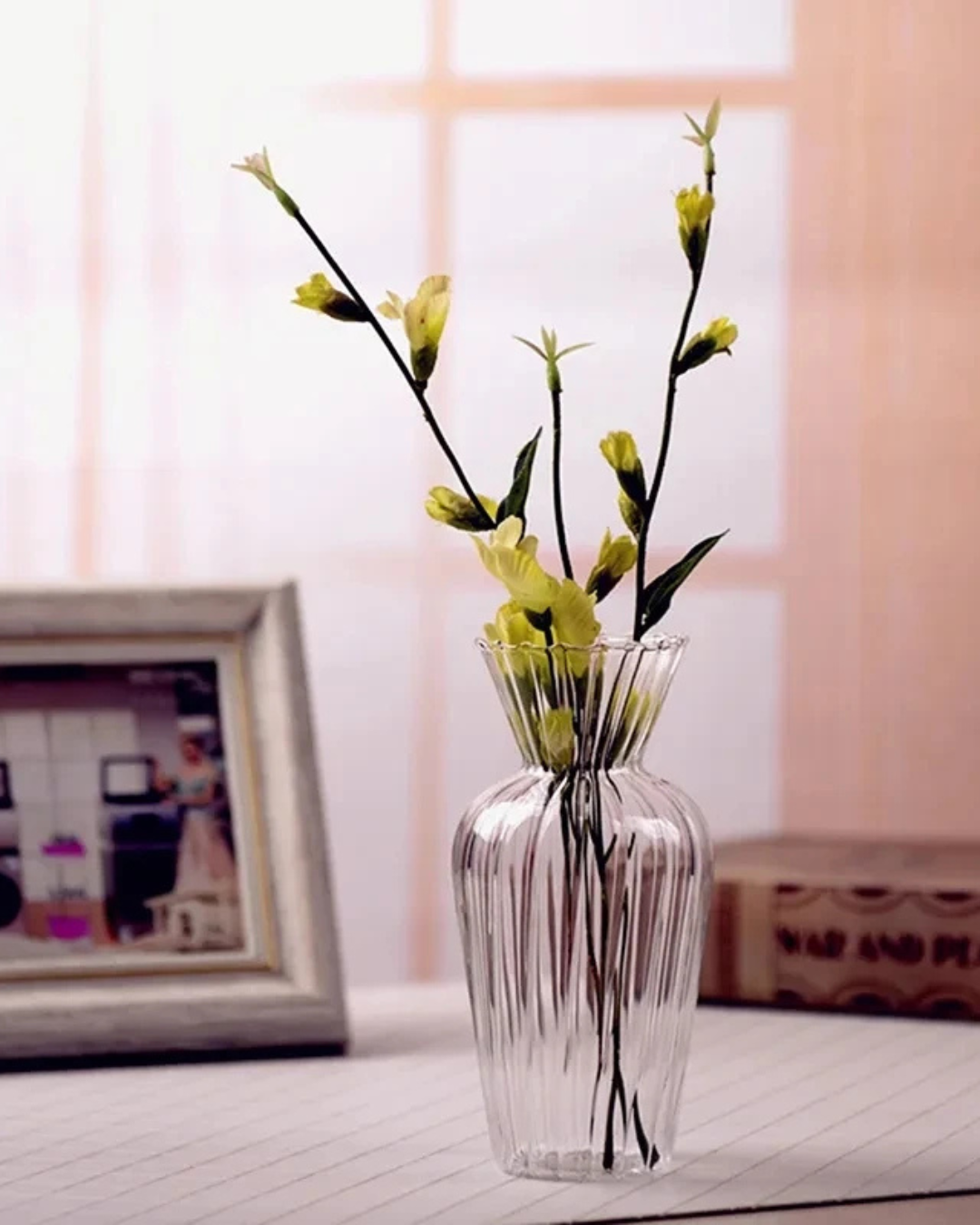 Vaso de Vidro para flores sob mesa com flor amarela dentro e quadro por perto
